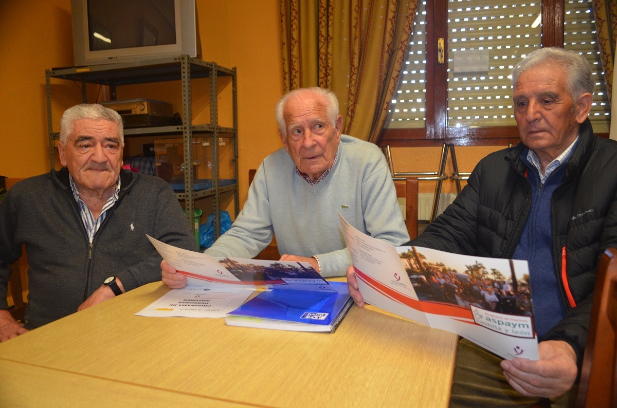 Tres personas mayores leyendo un folleto de ASPAYM