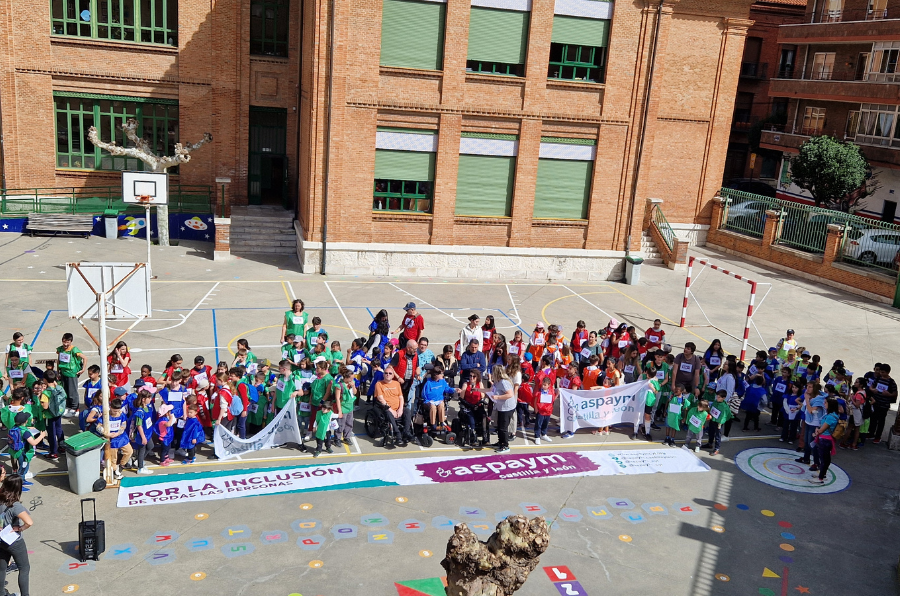 Alumnos y profesores del CEIP Isabel la Católica posan junto a la pancarta de ASPAYM CyL antes de la marcha