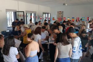 Grupo numeroso de jóvenes de distintos países participando en una dinámica en una sala de Valladolid, con banderas internacionales colgadas al fondo y documentos en las manos